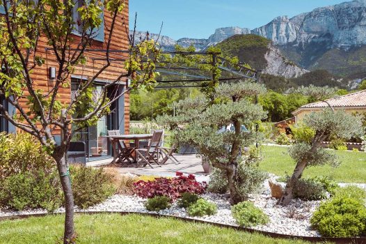 Création d’un espace bien-être extérieur avec l’installation d’un spa encastré à hauteur du sol, harmonieusement intégré dans un jardin paysager. Le spa est bordé par une terrasse en lames de bambou posée sur une structure métallique Terrassteel, assurant durabilité, résistance à l’humidité et finition soignée. Un mur en pierre naturelle vient structurer l’espace et renforcer l’ambiance authentique et chaleureuse. Des massifs paysagers complètent l’ensemble, avec notamment un olivier majestueux en élément central, apportant une touche méditerranéenne à la composition. Aménagement alliant confort, esthétisme et techniques modernes de construction extérieure. Ce projet illustre le savoir-faire d’un paysagiste et pisciniste en région Rhône-Alpes, intervenant à Valence, dans la Drôme et en Ardèche, pour des réalisations harmonieuses et techniques mêlant confort, tradition et modernité.