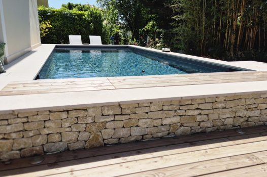 Piscine surélevée construite avec des panneaux modulaires Aquafeat, offrant une structure solide et durable pour un bassin hors-sol. L’ensemble est entouré d’un mur en pierre d’Eyzahut maçonné avec une finition en appareillage pierre sèche, assurant une parfaite intégration paysagère et une esthétique naturelle. La couverture du bassin est assurée par une bâche automatique immergée Aquagard, garantissant sécurité, protection et confort d’utilisation. À proximité immédiate, une terrasse contemporaine repose sur un lambourdage en structure métallique Terrassteel, avec un platelage en lames de bambou, matériau écologique et résistant. Aménagement extérieur complet alliant technicité, durabilité et design. Dupré la Tour piscine et paysage / Livron sur Drôme / Valence / Drôme Ardèche / paysagiste pisciniste