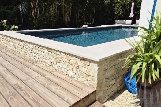 Piscine surélevée construite avec des panneaux modulaires Aquafeat, offrant une structure solide et durable pour un bassin hors-sol. L’ensemble est entouré d’un mur en pierre d’Eyzahut maçonné avec une finition en appareillage pierre sèche, assurant une parfaite intégration paysagère et une esthétique naturelle. La couverture du bassin est assurée par une bâche automatique immergée Aquagard, garantissant sécurité, protection et confort d’utilisation. À proximité immédiate, une terrasse contemporaine repose sur un lambourdage en structure métallique Terrassteel, avec un platelage en lames de bambou, matériau écologique et résistant. Aménagement extérieur complet alliant technicité, durabilité et design. Dupré la Tour piscine et paysage / Livron sur Drôme / Valence / Drôme Ardèche / paysagiste pisciniste