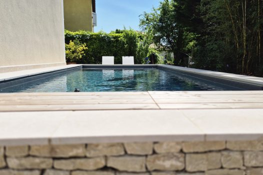 Piscine surélevée construite avec des panneaux modulaires Aquafeat, offrant une structure solide et durable pour un bassin hors-sol. L’ensemble est entouré d’un mur en pierre d’Eyzahut maçonné avec une finition en appareillage pierre sèche, assurant une parfaite intégration paysagère et une esthétique naturelle. La couverture du bassin est assurée par une bâche automatique immergée Aquagard, garantissant sécurité, protection et confort d’utilisation. À proximité immédiate, une terrasse contemporaine repose sur un lambourdage en structure métallique Terrassteel, avec un platelage en lames de bambou, matériau écologique et résistant. Aménagement extérieur complet alliant technicité, durabilité et design. Dupré la Tour piscine et paysage / Livron sur Drôme / Valence / Drôme Ardèche / paysagiste pisciniste