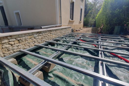 Piscine surélevée construite avec des panneaux modulaires Aquafeat, offrant une structure solide et durable pour un bassin hors-sol. L’ensemble est entouré d’un mur en pierre d’Eyzahut maçonné avec une finition en appareillage pierre sèche, assurant une parfaite intégration paysagère et une esthétique naturelle. La couverture du bassin est assurée par une bâche automatique immergée Aquagard, garantissant sécurité, protection et confort d’utilisation. À proximité immédiate, une terrasse contemporaine repose sur un lambourdage en structure métallique Terrassteel, avec un platelage en lames de bambou, matériau écologique et résistant. Aménagement extérieur complet alliant technicité, durabilité et design. Dupré la Tour piscine et paysage / Livron sur Drôme / Valence / Drôme Ardèche / paysagiste pisciniste