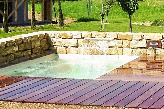 Création d’un espace bien-être extérieur avec l’installation d’un spa encastré à hauteur du sol, harmonieusement intégré dans un jardin paysager. Le spa est bordé par une terrasse en lames de bambou posée sur une structure métallique Terrassteel, assurant durabilité, résistance à l’humidité et finition soignée. Un mur en pierre naturelle vient structurer l’espace et renforcer l’ambiance authentique et chaleureuse. Des massifs paysagers complètent l’ensemble, avec notamment un olivier majestueux en élément central, apportant une touche méditerranéenne à la composition. Aménagement alliant confort, esthétisme et techniques modernes de construction extérieure. Ce projet illustre le savoir-faire d’un paysagiste et pisciniste en région Rhône-Alpes, intervenant à Valence, dans la Drôme et en Ardèche, pour des réalisations harmonieuses et techniques mêlant confort, tradition et modernité.